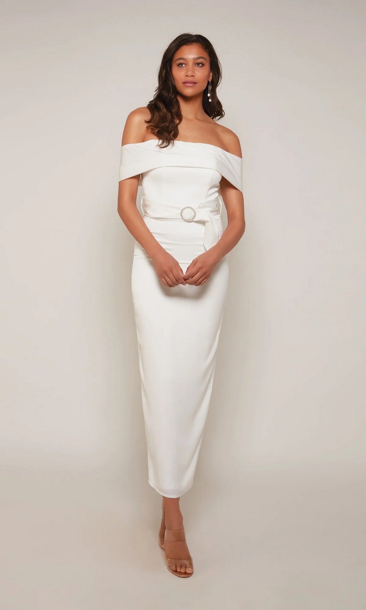 Woman wearing the Tea Length Formal Dress: Alyce 70041 in Diamond White with off-the-shoulder, belt and buckle detail, paired with tan heeled sandals—an ideal wedding guest dress against a plain light background.